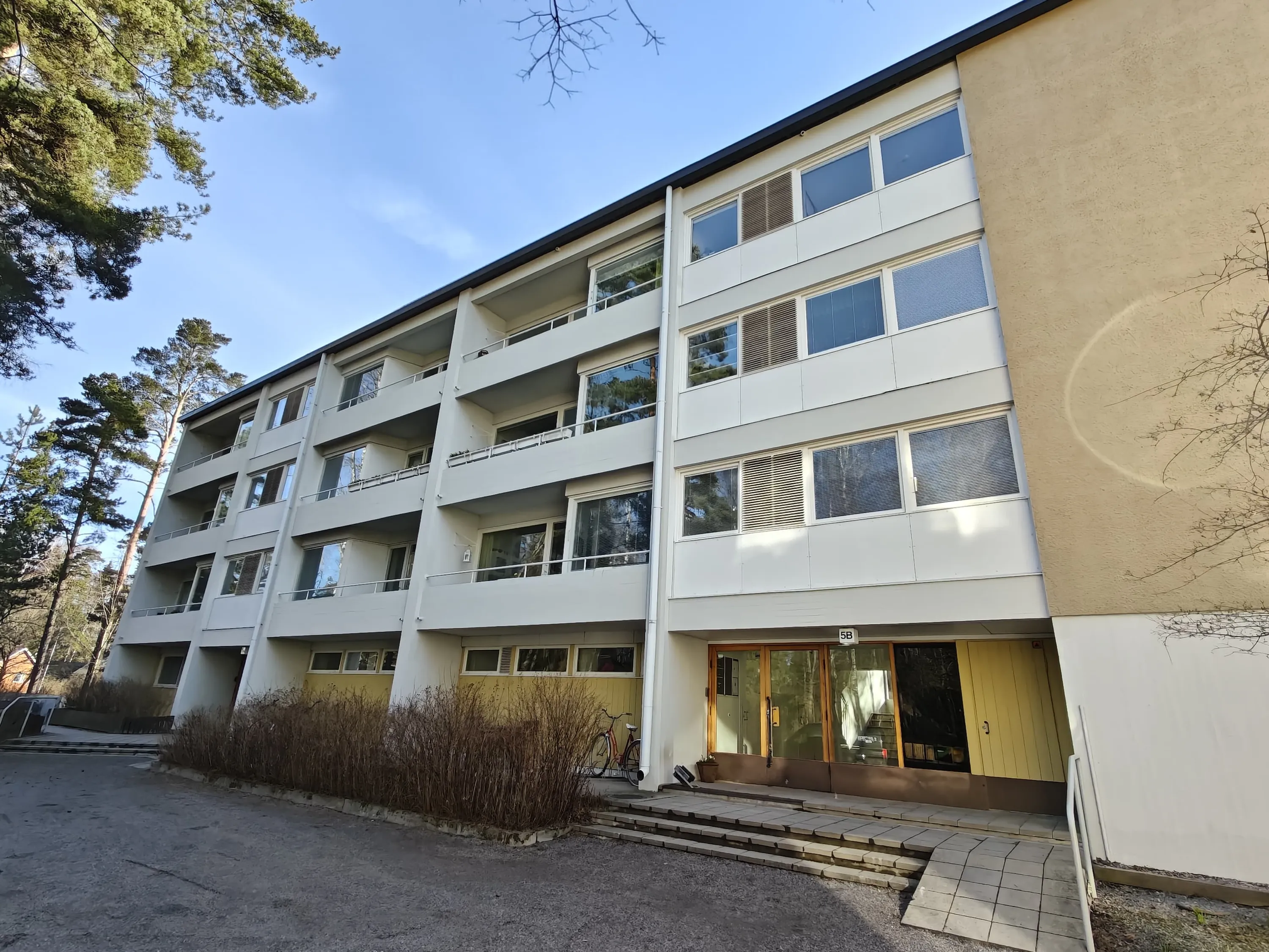 Matala asuintalo, jossa on parvekkeet ja suuret ikkunat, valaistuna auringonvalolla.