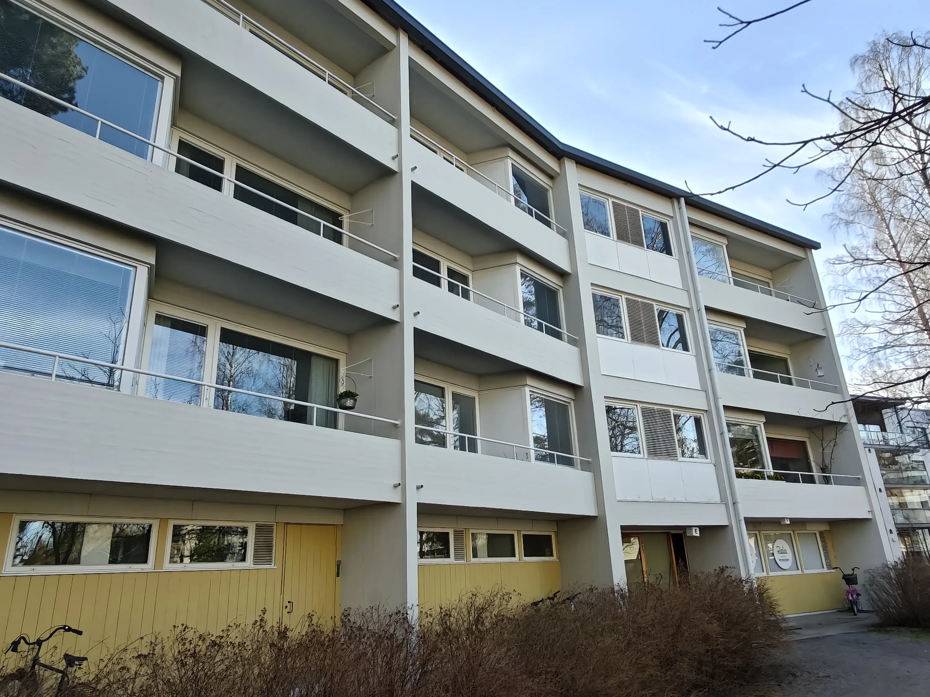 Vaaleanharmaa kerrostalo, jossa on keltaisia yksityiskohtia ja parvekkeet, valoisa sää.