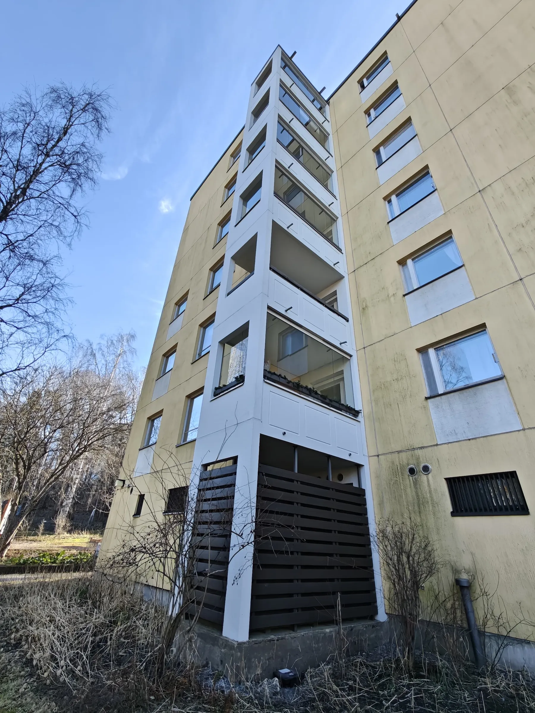 Korkea kerrostalo, jossa on keltaiset seinät ja valkoinen parveketorni, kuvattu alhaalta ylöspäin aurinkoisena päivänä.