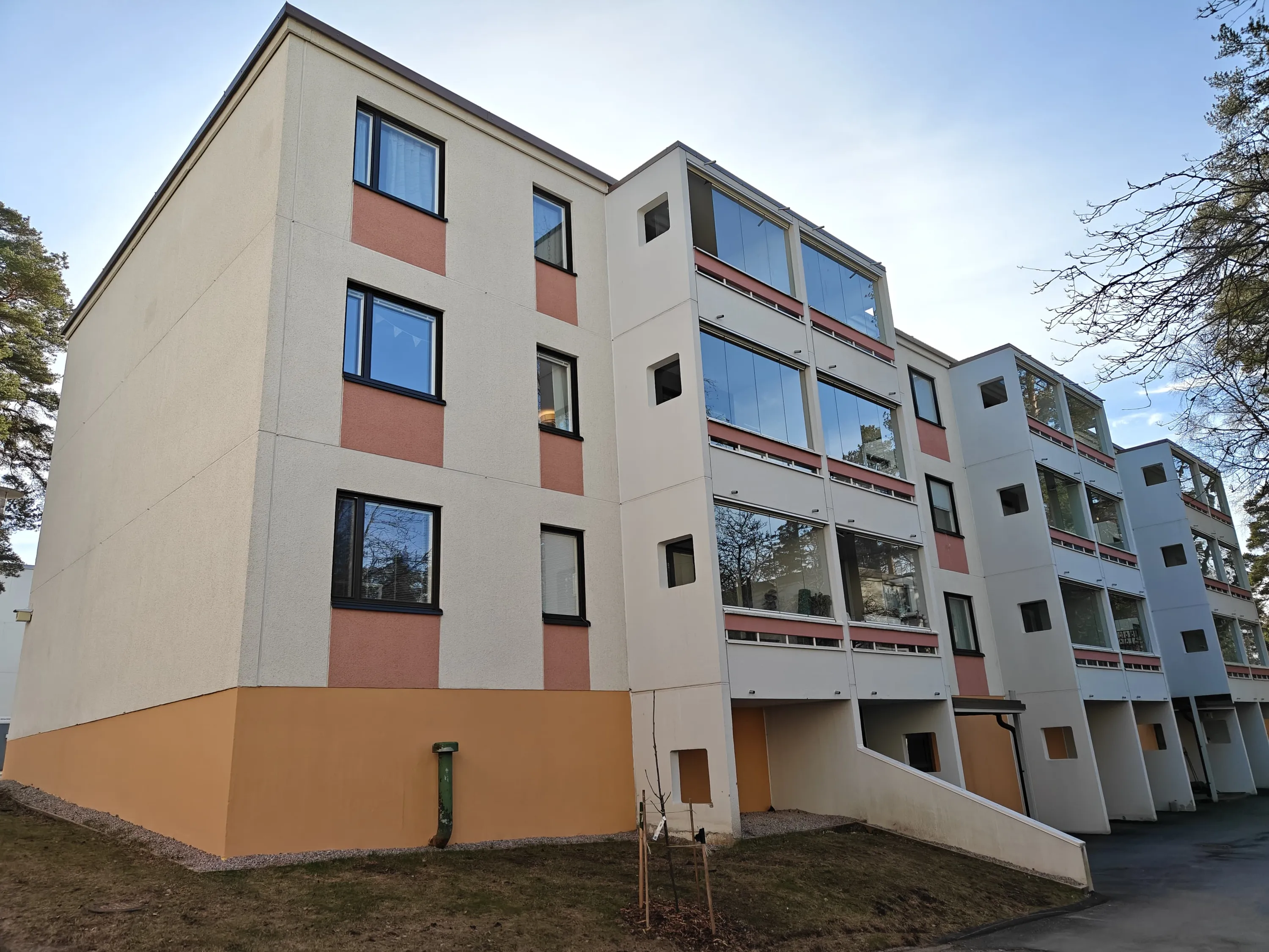 Matala kerrostalo, jossa on beige julkisivu, punaruskeita yksityiskohtia ja lasitetut parvekkeet, valaistu päivänvalossa.
