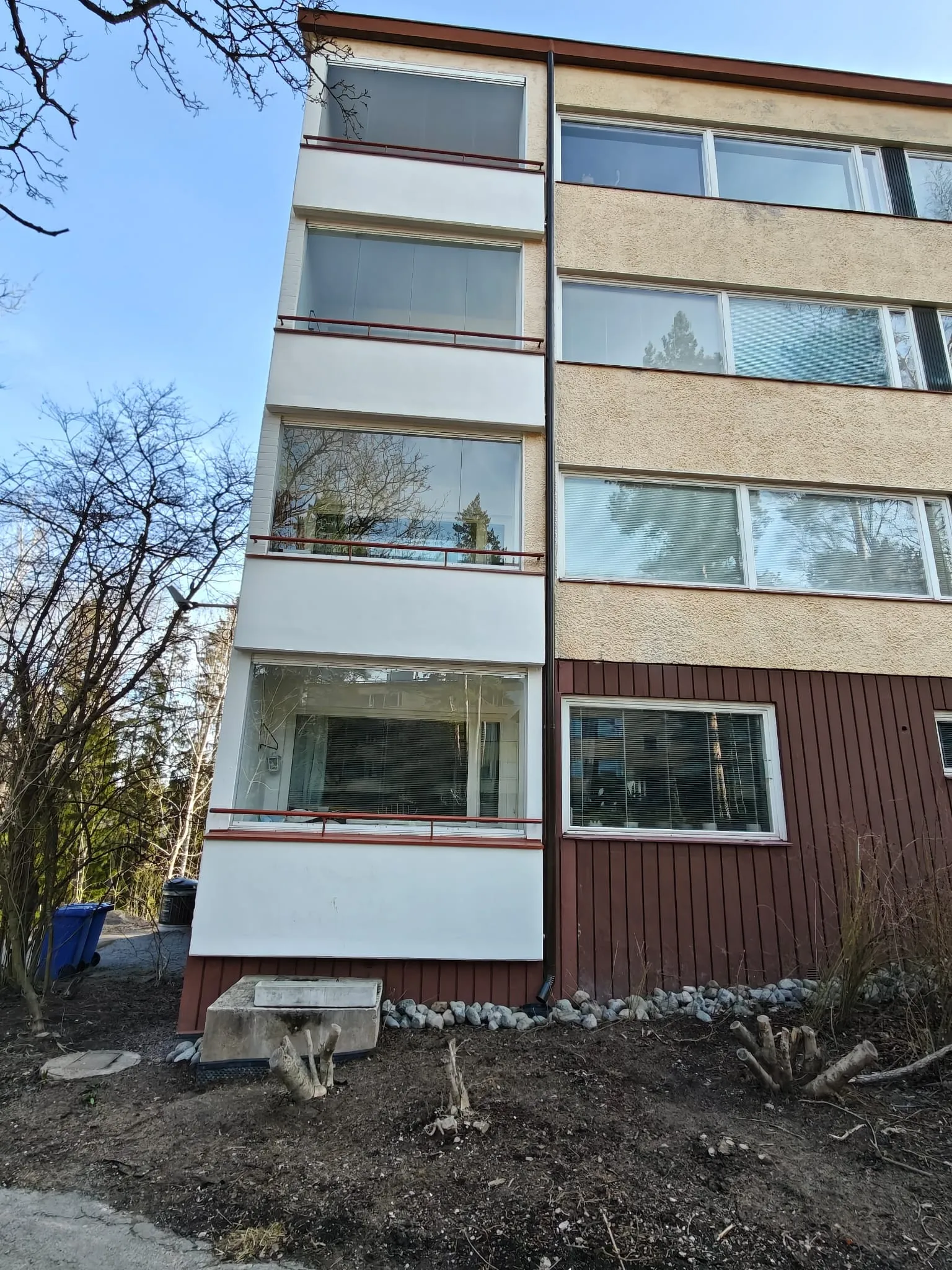 Kerrostalo, jossa on lasitetut parvekkeet ja ruskea puuverhoilu alaosassa, valaistu auringonvalolla.