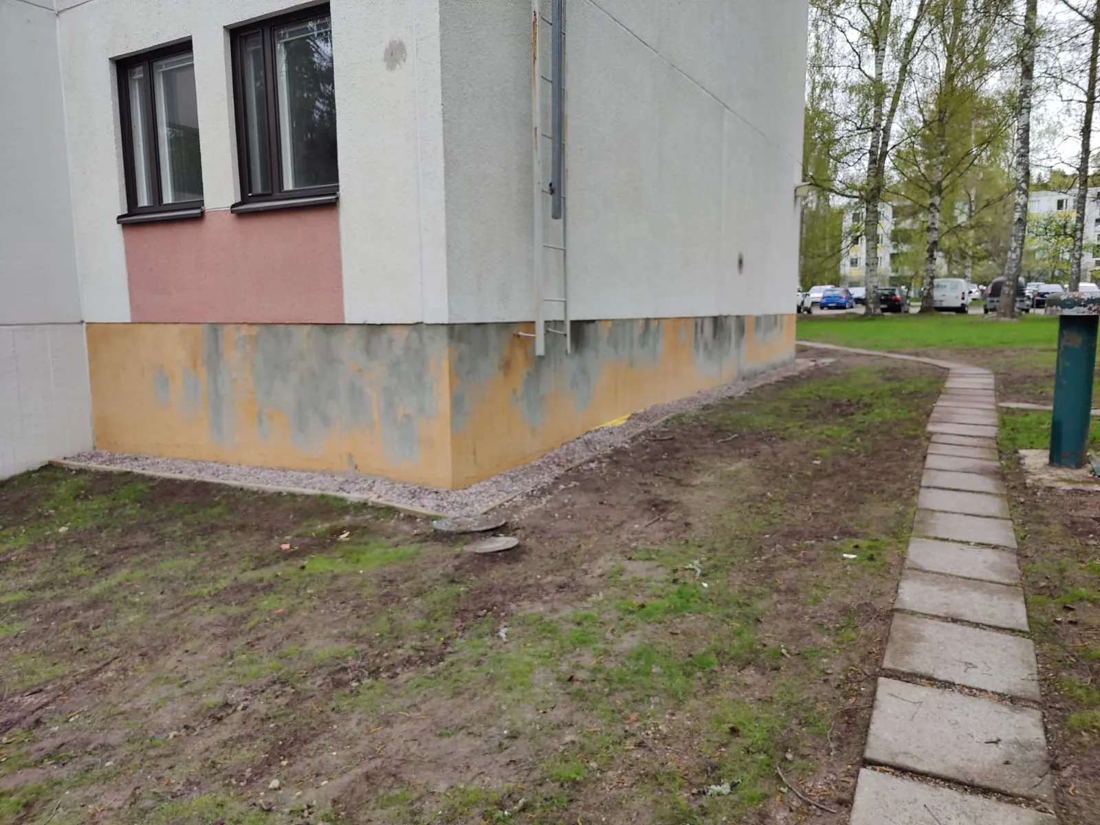 Ulkokuva rakennuksesta, jossa on ikkunat, tikkaat ja kivetty polku, valaistus on luonnollinen.