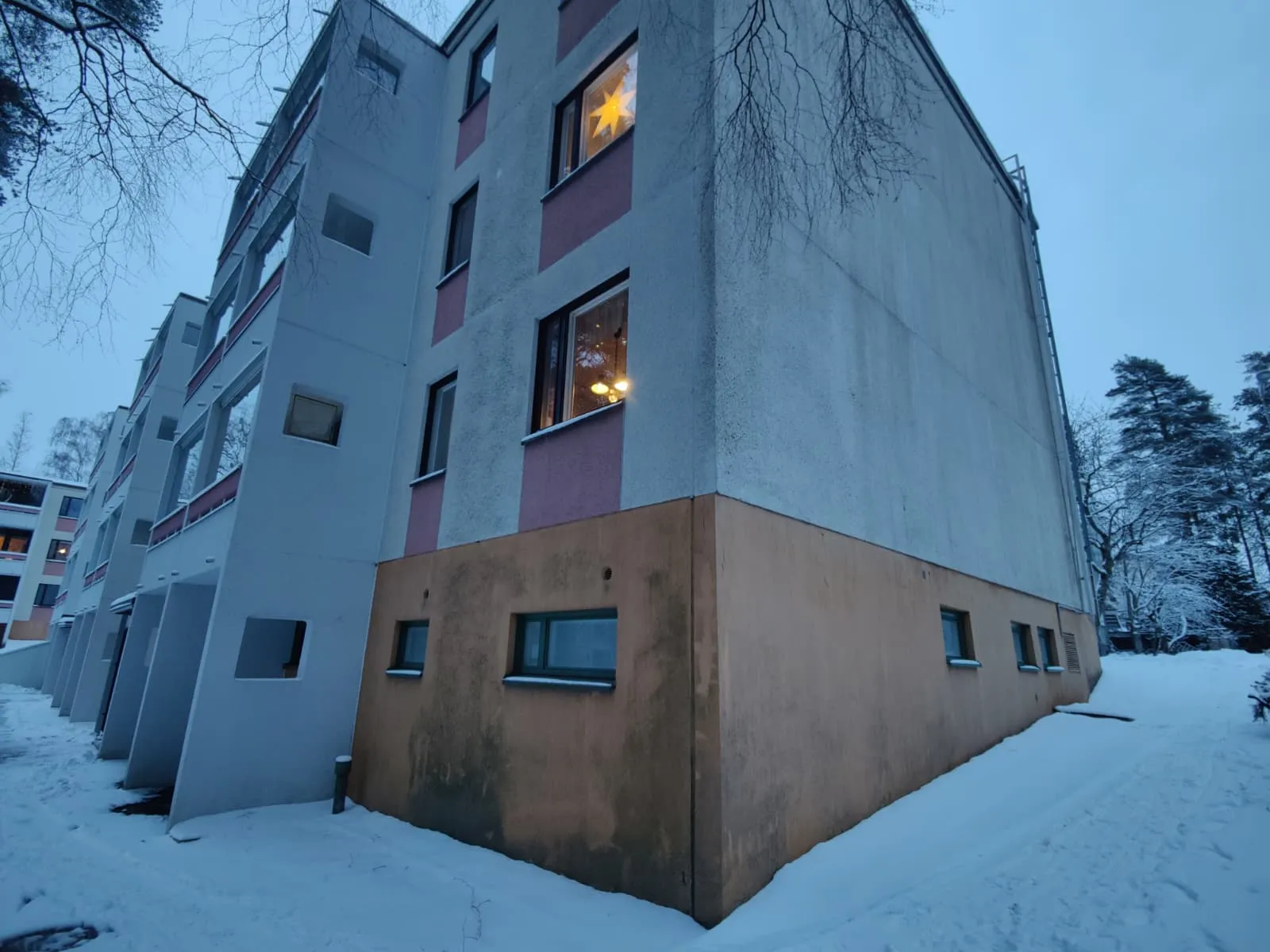 Kerrostalo lumisessa maisemassa, ikkunassa tähti, harmaa sää.