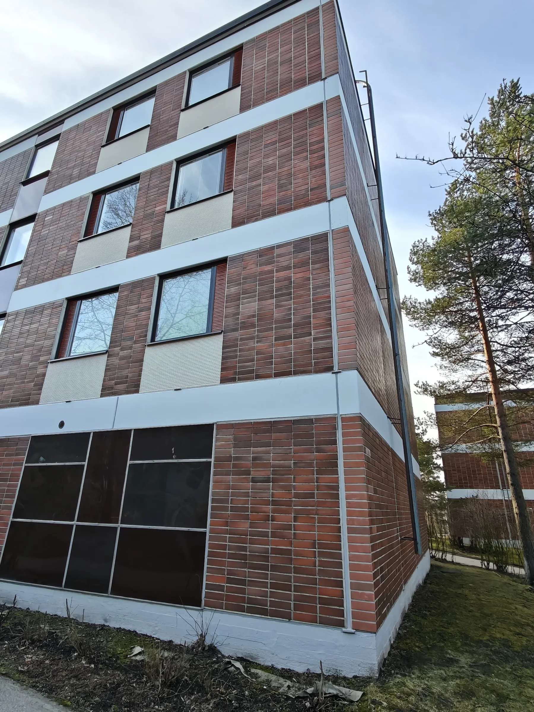 Kulmasta otettu kuva tiilirakennuksesta, jossa on ikkunoita ja valkoisia korostuksia, valaistus on luonnollinen.
