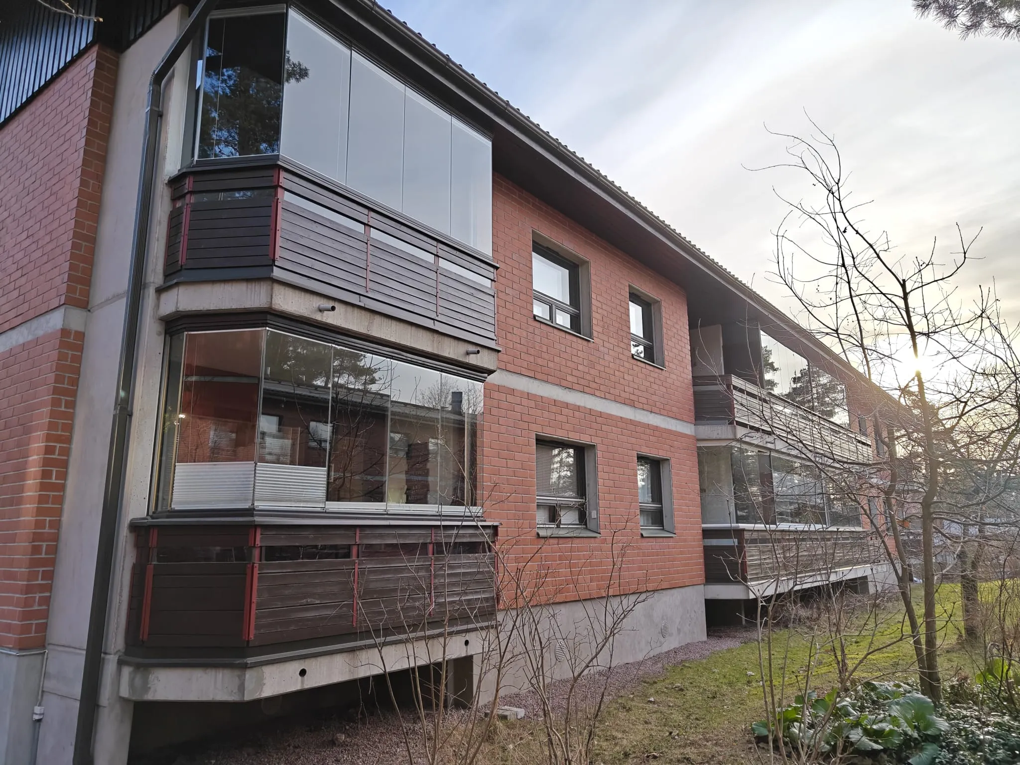Punatiilinen kerrostalo, jossa on lasitetut parvekkeet ja ruskeat puukaiteet, valoisa sää.