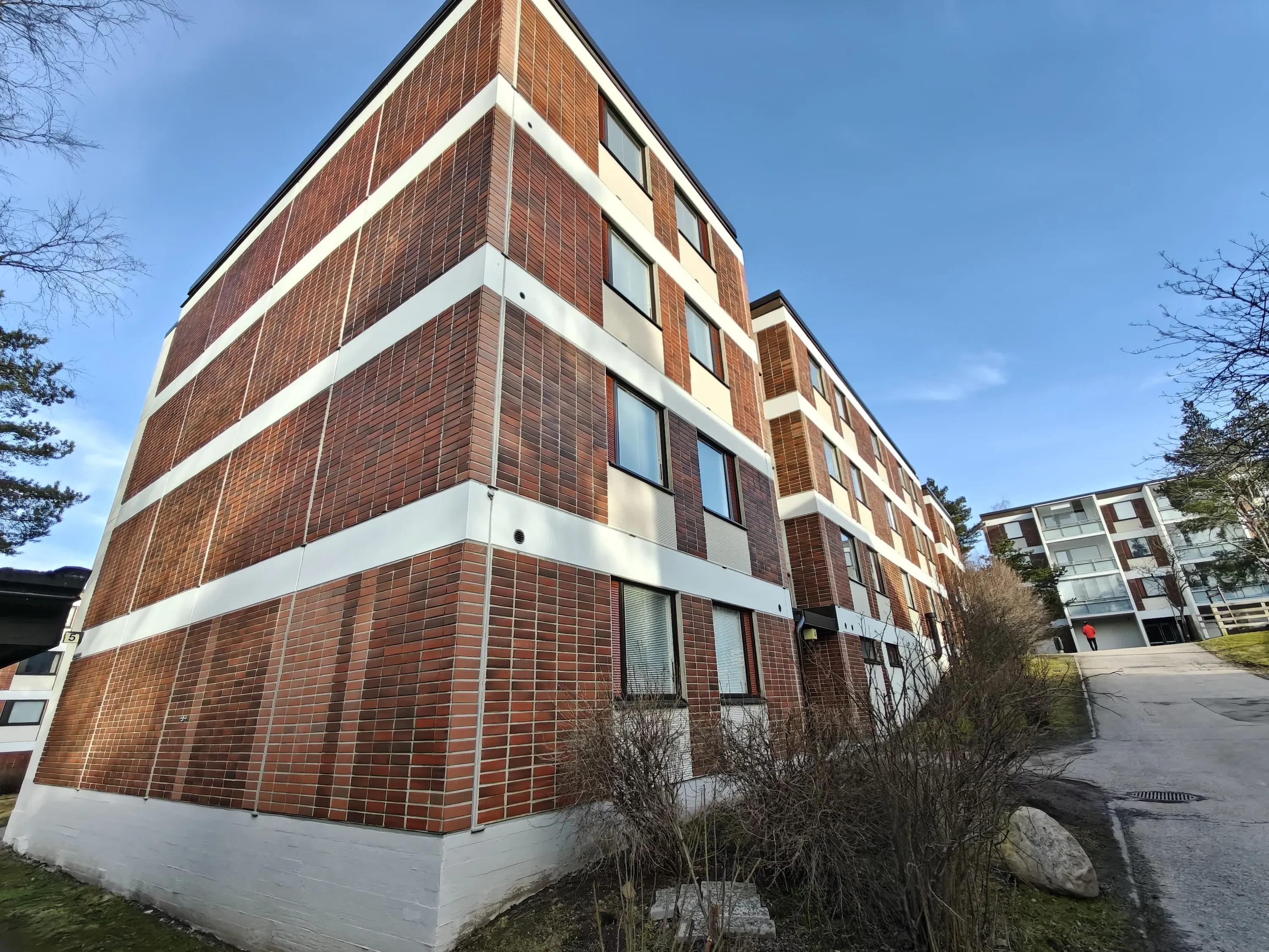 Matala kulma punatiilitalosta, jossa on valkoiset korostukset ja sininen taivas.